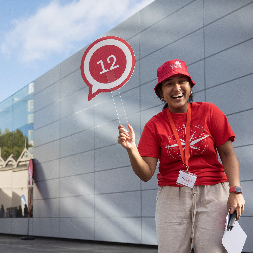 Student in red UniGuide merch holding paddle with number 12 on it