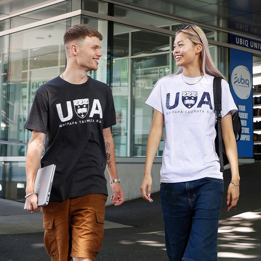 Two students walking on campus wearing UoA tees.