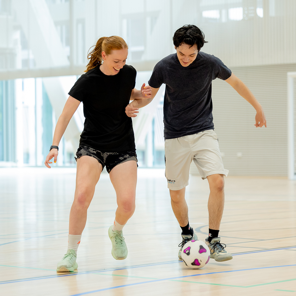 Two students playing football in a sports hall