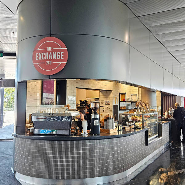 The Exchange café counter at the University of Auckland, with coffee machines, cabinet food, and staff serving inside a curved kiosk space.