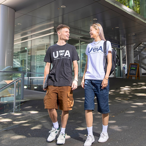 Two students posing in front of the camera with UoA merch